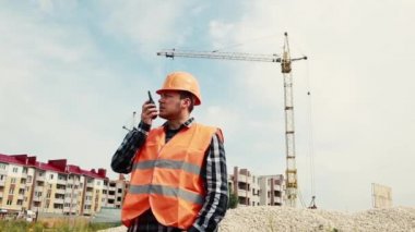 İnşaatçı telsizle bir inşaat alanının arka planına bakarak konuşuyor..