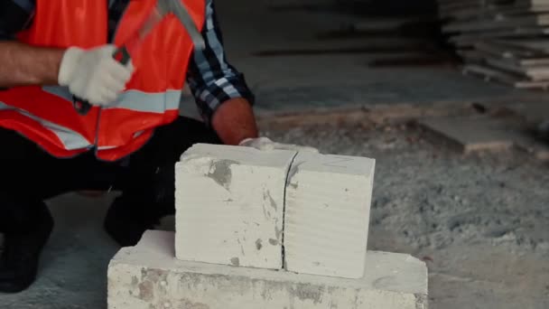 Um construtor em um colete laranja está martelando em uma pedra . — Vídeo de Stock