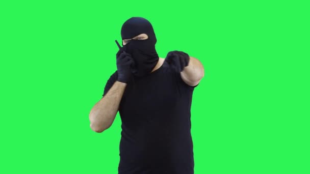 Um homem em uma balaclava falando em um walkie-talkie faz uma escolha com a mão, fundo de tela verde — Vídeo de Stock