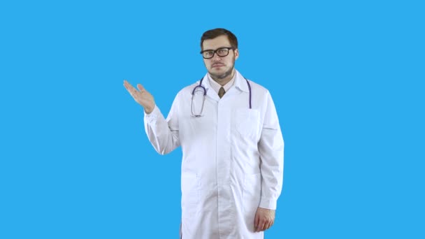 Un médico con un abrigo médico blanco y gafas se muestra con una mano para mirar aquí . — Vídeo de stock