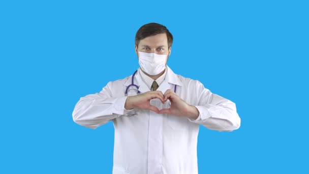 Arzt in Arztkittel und Maske zeigt ein Herz mit der Hand. — Stockvideo