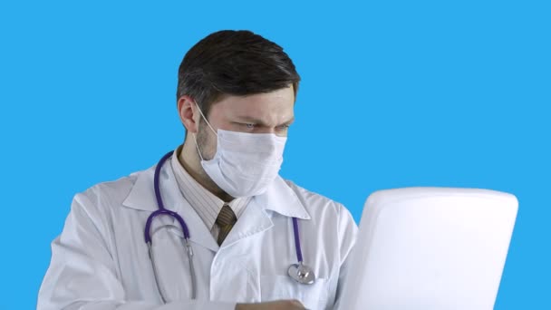 Un medico in abito medico e maschera inserisce i dati in un computer portatile . — Video Stock