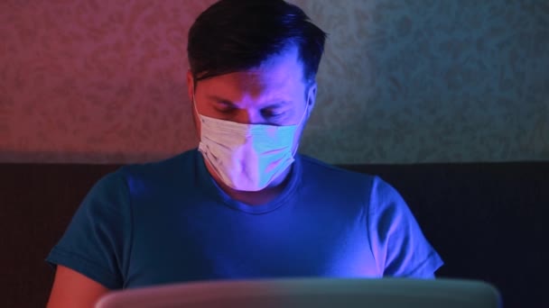 Un uomo mascherato in quarantena lavora a distanza dietro un portatile . — Video Stock