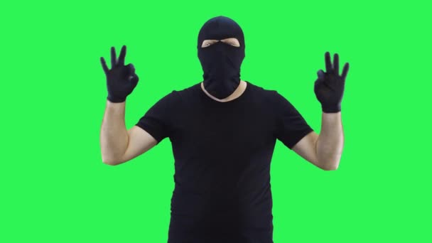 Мужчина в балаклаве показывает двумя руками все в порядке, зеленый фон — стоковое видео