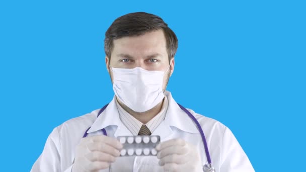 Ένας γιατρός με ένα ιατρικό παλτό και μάσκα κρατά ένα πακέτο χάπια και με τα δύο χέρια. — Αρχείο Βίντεο