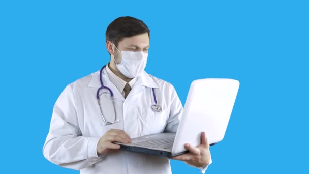 A doctor in a medical coat and mask is talking via video link on a laptop. — Stock Video