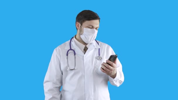 Un médecin en blouse médicale et masque parle au téléphone via un lien vidéo . — Video