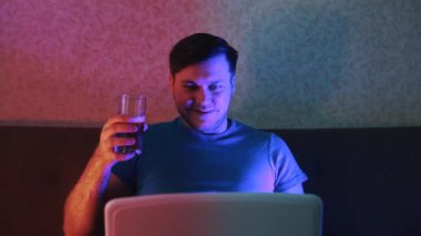 Genç bir adam bir arkadaşıyla laptopta iletişim kuruyor ve bira içiyor..