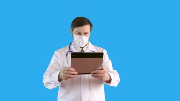 Mężczyzna w płaszczu medycznym i masce komunikuje się przez łącze wideo na tablecie.. — Wideo stockowe