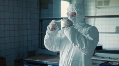Koruyucu takım elbiseli, maske ve gözlüklü bir adam elinde bir test tüpü tutuyor..