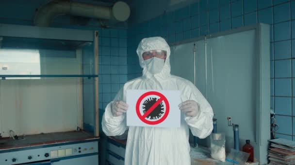 Ένας άντρας με προστατευτική στολή και προστατευτική μάσκα που δείχνει με ένα σημάδι να σταματήσει τον κορωναϊό. Σταματήστε την επιδημία coronavirus. — Αρχείο Βίντεο