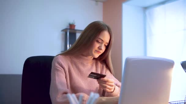 Młoda dziewczyna pracuje przy laptopie, siedzi przy stole w pracy zdalnej, wpisuje dane z karty kredytowej.. — Wideo stockowe