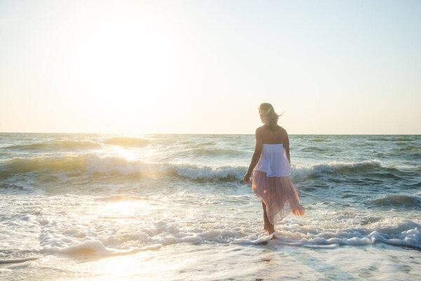 молодая женщина в белом платье прогуливается по морскому пляжу 