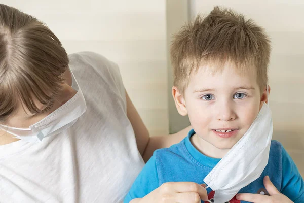 Mom takes off or puts on a medical mask for the child, the boy looks with hope into the camera