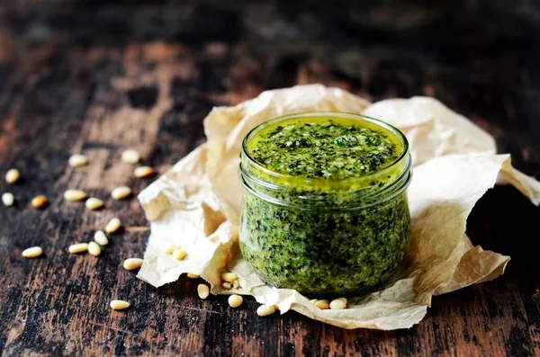 Koyu arkaplanda cam bir kavanozda pesto sosu.