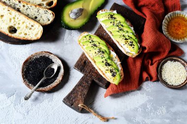 Avokado, peynir, chia tohumu ve gri arkaplanda susam tohumlu sandviç.