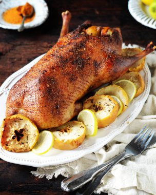 Koyu ahşap bir masada elmalı ve limonlu geleneksel fırında ördek.