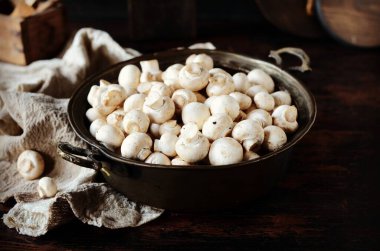 Koyu ahşap bir masada, demir kasede taze çiğ şampiyonlar.