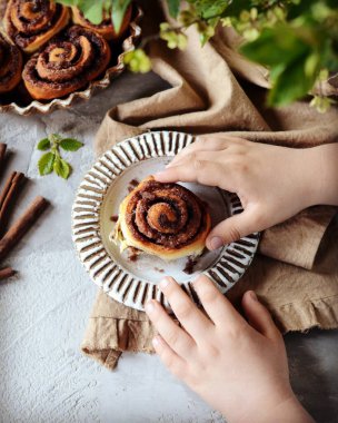 Gri masadaki bir çocuğun ellerinde tarçınlı çörekler