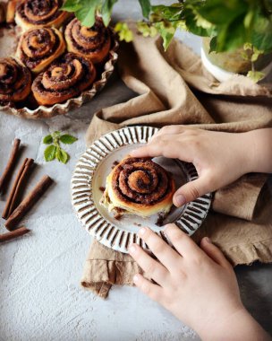 Gri masadaki bir çocuğun ellerinde tarçınlı çörekler