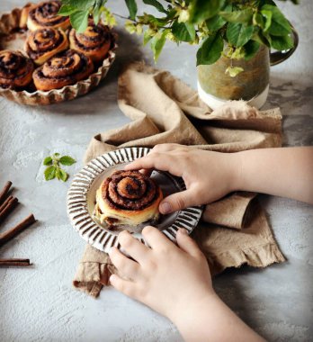 Gri masadaki bir çocuğun ellerinde tarçınlı çörekler