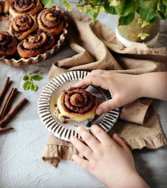 Gri masadaki bir çocuğun ellerinde tarçınlı çörekler
