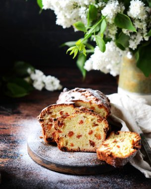 Kuru üzümlü kremalı pasta koyu arkaplanlı, leylak çiçekli bir kesim tahtası.
