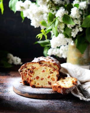 Kuru üzümlü kremalı pasta koyu arkaplanlı, leylak çiçekli bir kesim tahtası.