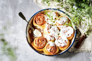 Tarçınlı çörekler fırında krem peynirli, gri bir arka planda.