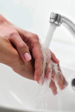 Kadın musluğun altında sabun ve ellerini yıkıyor. Temizlikçi Eller. Hijyen. Pembe manikür. Yumuşak odak