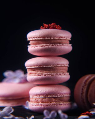 Ahududulu Fransız kurabiyeleri, siyah arka planda, leylak çiçekleriyle süslenmiş, dikey makro, yumuşak odaklı.