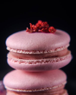 Ahududulu Fransız kurabiyeleri, siyah arka planda, leylak çiçekleriyle süslenmiş, dikey makro, yumuşak odaklı.