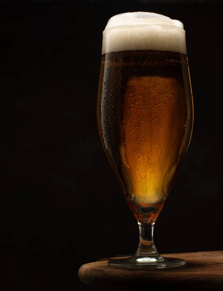 Bière fraîche dans un verre sur table en bois sur fond noir . — Photo