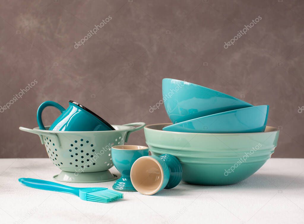 Various blue kitchen dishes:plate,colander,egg stand,cup and ceramic bowls on grey background.Close up.