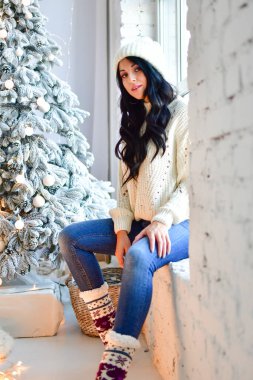 Kız Noel ağacını pencerenin önündeki çelenklerle süslüyor.