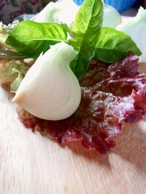 Güneşin altında tahta bir masada soğan, fesleğen ve marul kes..