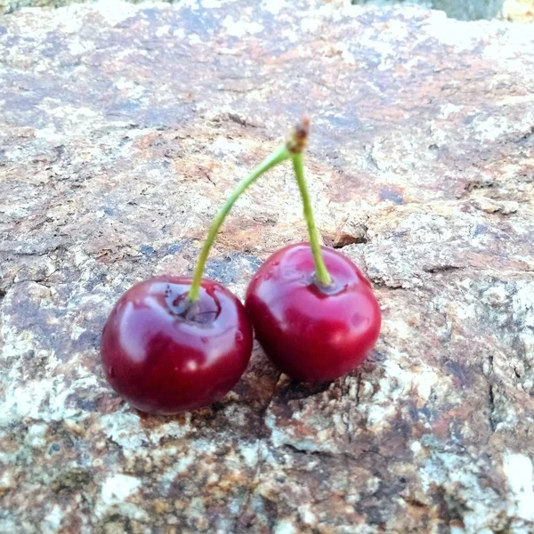 Two raw sweet cherries isolated on an old stone — Stock Photo, Image