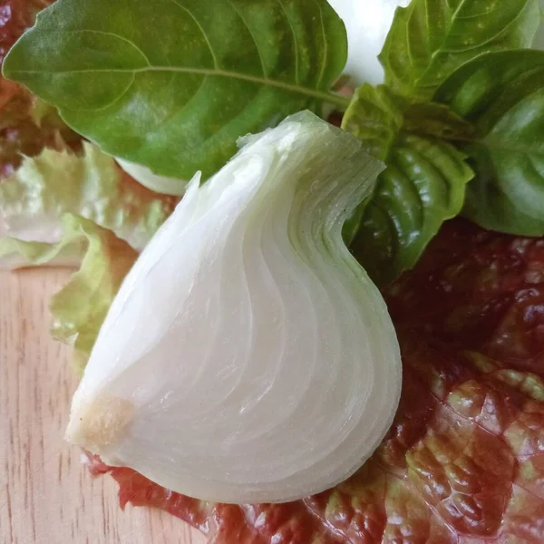 Güneşin altında tahta bir masada soğan, fesleğen ve marul kes..