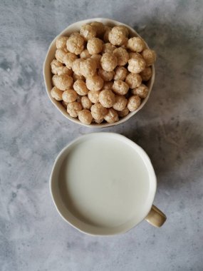 Bej bir fincanda karabuğday topları ve bir fincan süt.