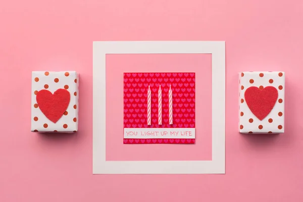 Χειροποίητα τυλιγμένα κουτιά δώρου, κόκκινες καρδιές και κεριά σε ροζ πλάτη — Φωτογραφία Αρχείου