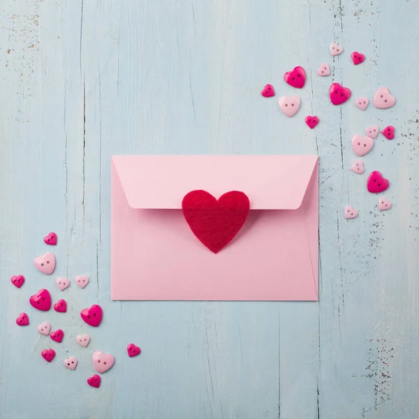 Envelope de papel rosa com coração vermelho no fundo azul de madeira — Fotografia de Stock