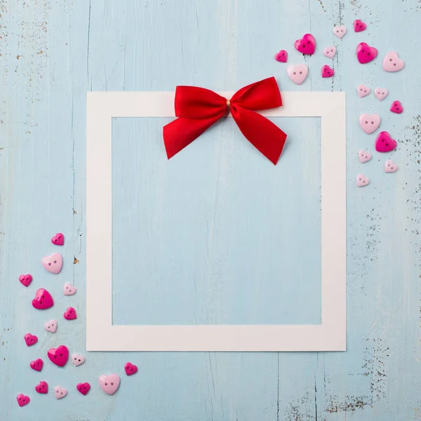 Arco vermelho artesanal e pequenos corações rosa no fundo azul de madeira — Fotografia de Stock