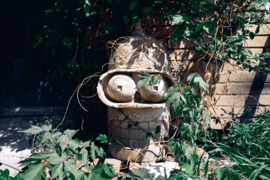 Futurama çizgi filminden bir Bender robotunun beton taş kafası yeşil bitkilerin arasında duruyor.