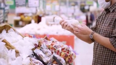 Tıbbi koruyucu maskeli genç bir adam süpermarketten sebze seçer. COVID 19 Nefsi müdafaa