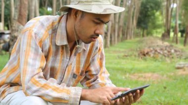 Kauçuk ağacı bahçede dijital tablet kullanan genç bahçıvan adam