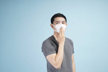 Korona virüsüne karşı yüz koruyucu maskeli ve dezenfekte spreyli Asyalı genç adam, ya da kış boyunca grip veya soğuk algınlığını önler.