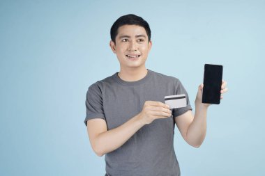 Kredi kartıyla alışveriş yapan genç Asyalı bir adam. Stüdyodaki izole gri arka planda bir şeyler alıp satıyor.