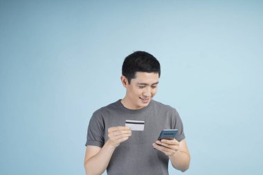 Kredi kartıyla alışveriş yapan genç Asyalı bir adam. Stüdyodaki izole gri arka planda bir şeyler alıp satıyor.