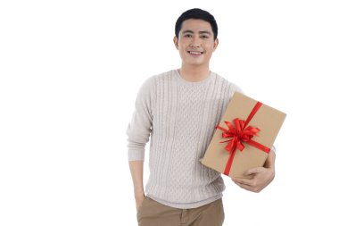 Gri arka planda örülü süveter giyen Asyalı genç adam kırmızı kurdele hediye kutusu veriyor.