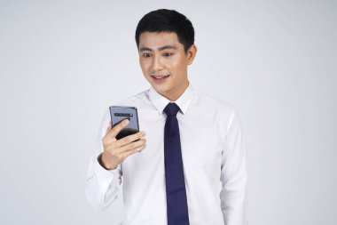 Gülümseyen Asyalı iş adamı gri arka planda tek başına duruyor, cep telefonu kullanıyor.